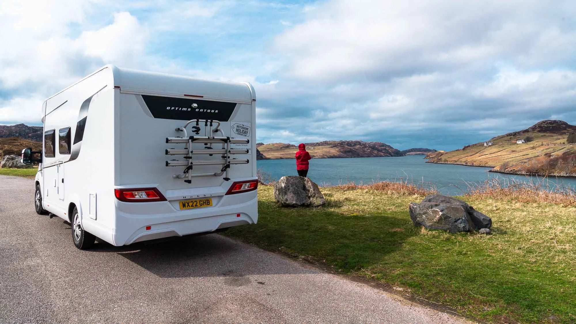 White caravan parked on a road with a scenic view of a lake and mountains in the background.