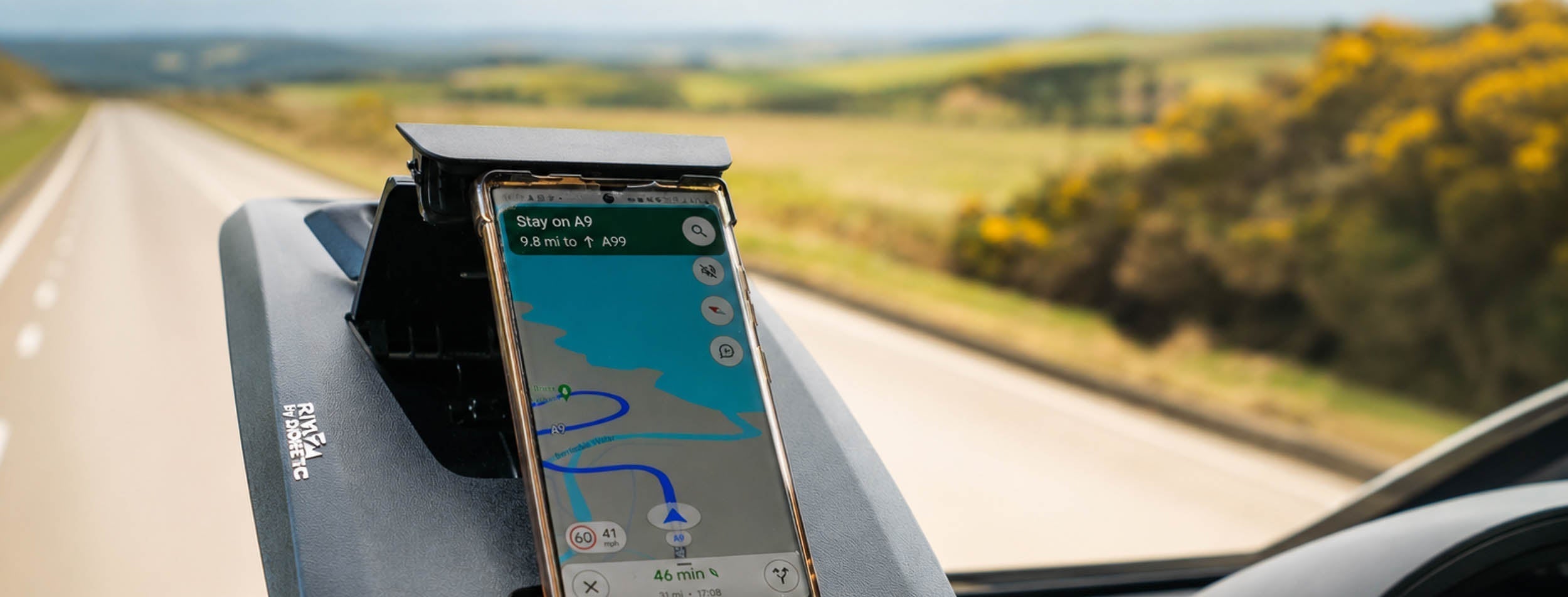 Phone mounted on a motorhome dashboard with a navigation app on the screen and landscape view outside