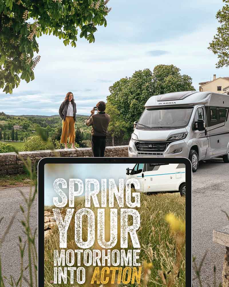 Two people taking a photo of a motorhome with a scenic background, overlaid with text 'Spring your motorhome into action'.